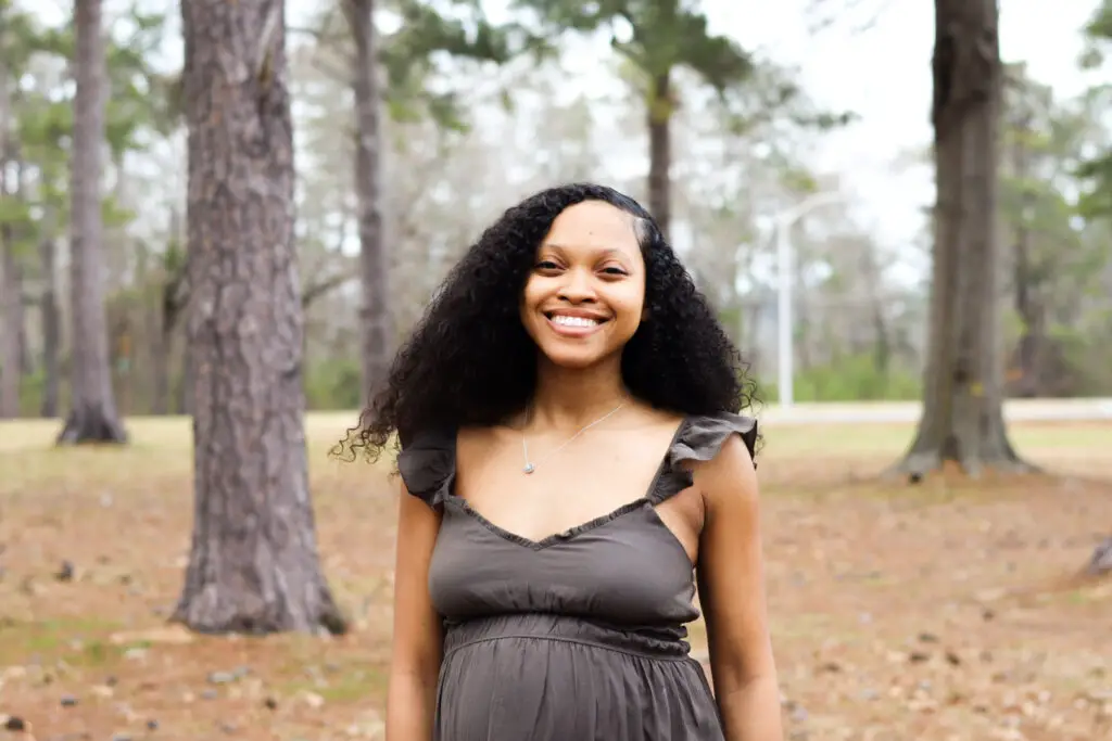 women with curly hair smiling outside next to trees