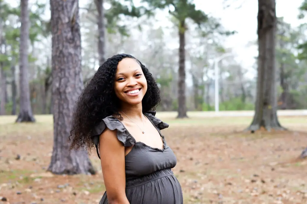 woman with curly hair in gree dress standing outside smiling