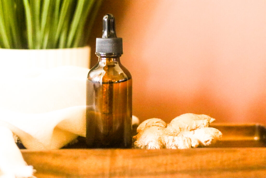ginger oil essential oil on wooden tray next to ginger root