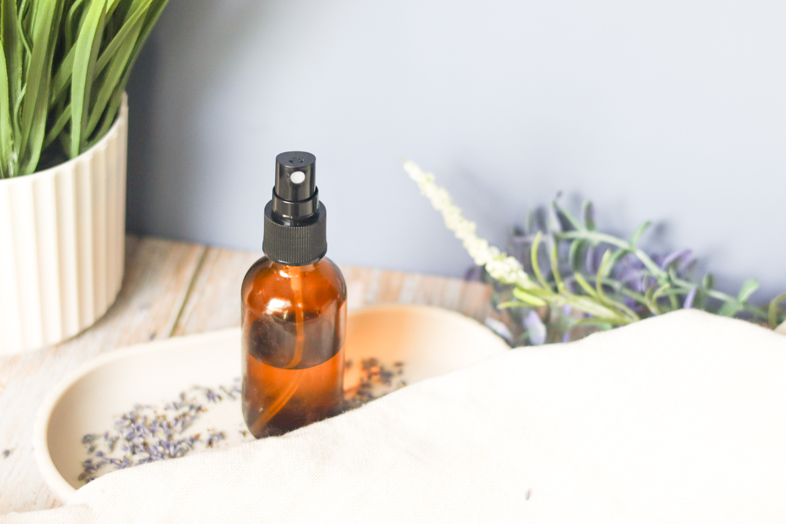 lavender room mist on white tray next to white linen