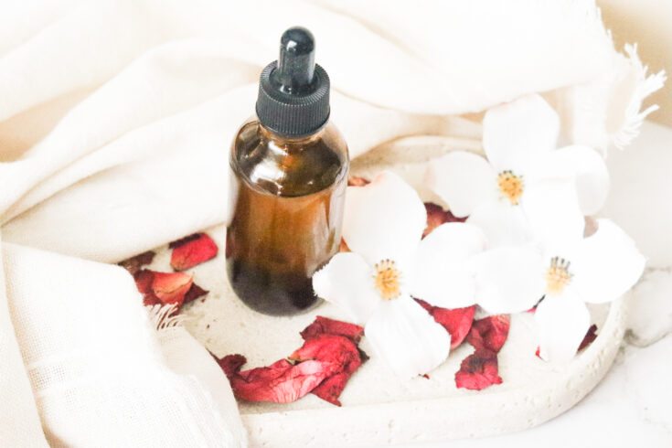 massage oil for boobs next to roses and in an amber glass bottle